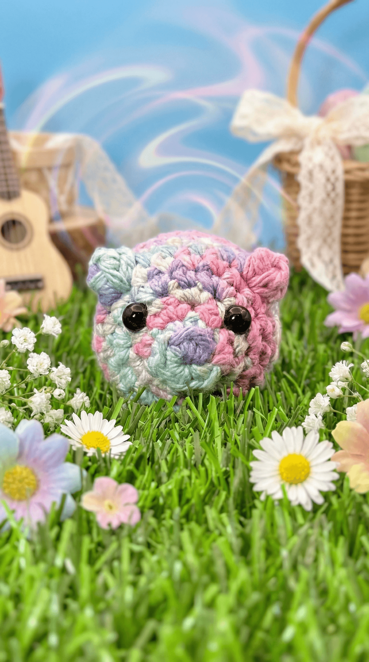 Pastel rainbow crocheted pig with black button eyes sitting on artificial grass surrounded by white and pink daisies. Handmade amigurumi in soft pink, purple, mint green variegated yarn.