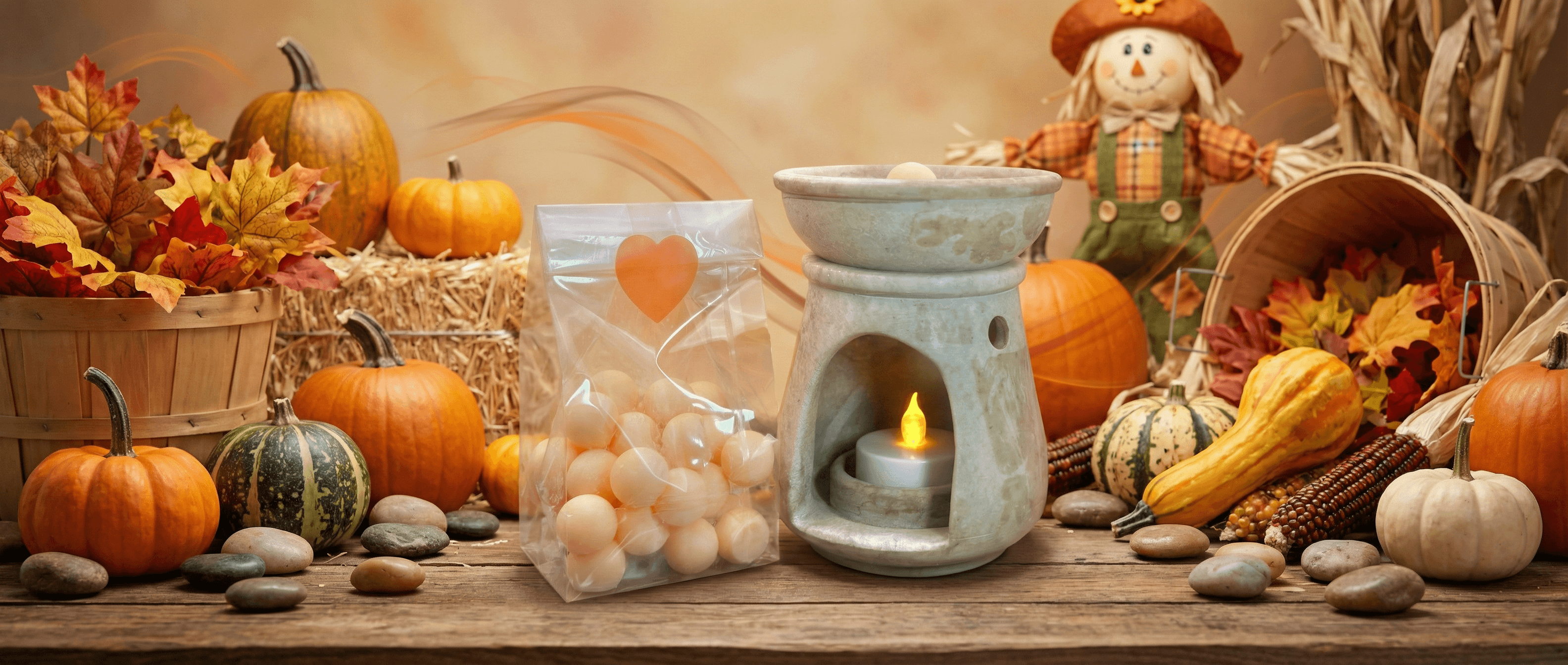 Autumn display with a ceramic wax melt warmer, clear bag of peach-colored wax melt balls with orange heart label, surrounded by pumpkins, gourds, fall leaves, and decorative scarecrow.