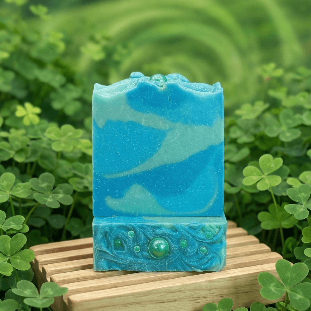 Rectangular bar with swirled blue and aqua layers, topped with decorative ocean wave textured base embedded with green sphere embeds. Displayed on wooden slats with clover plants.