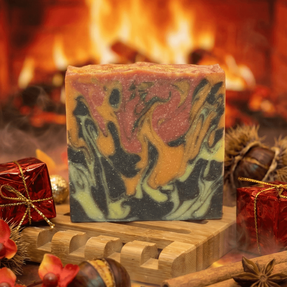 Marbled soap bar with flame-like swirls in orange, red, charcoal, and olive green, displayed on a wooden soap dish with fireplace, chestnuts, and wrapped gifts in background.