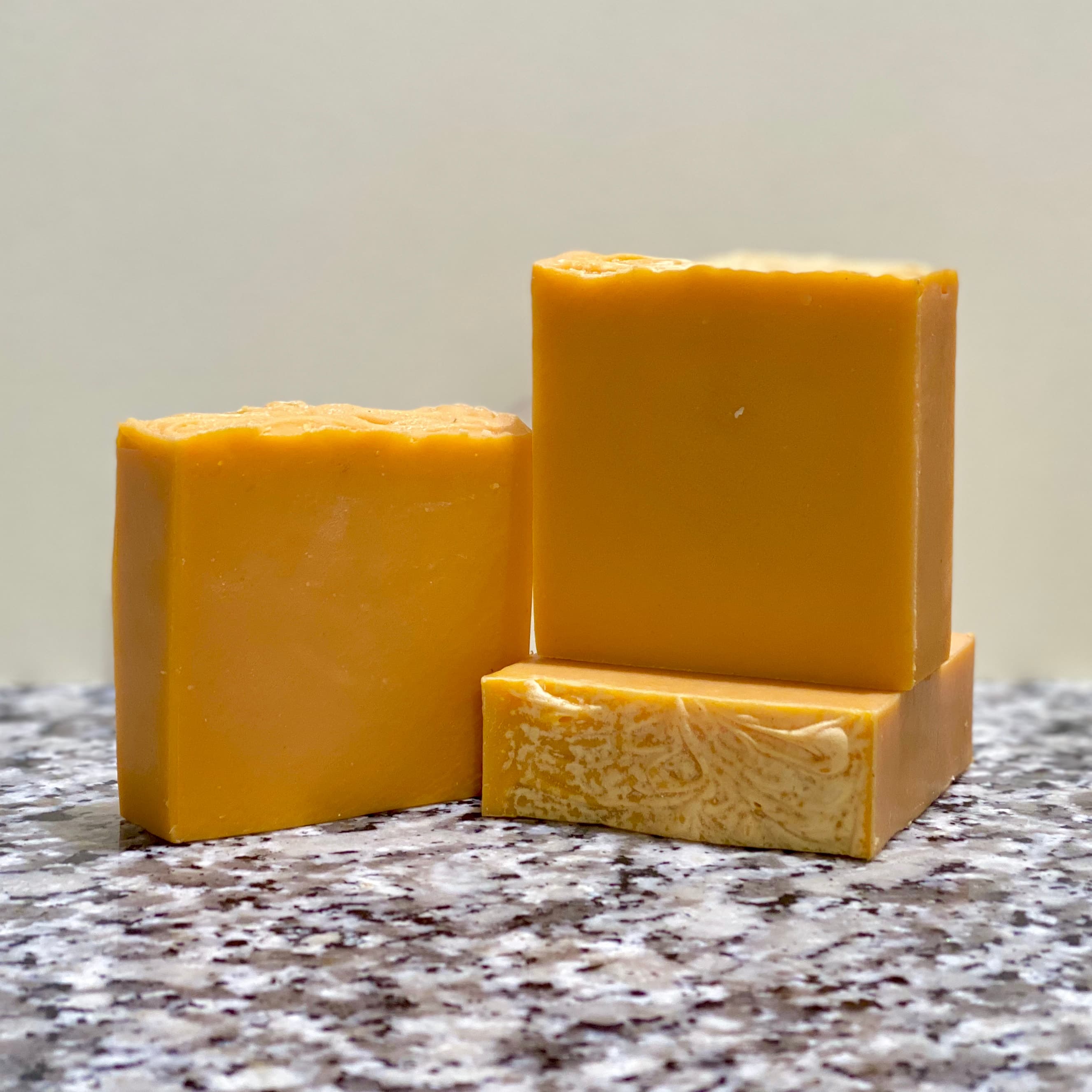 Three golden-orange rectangular bars with smooth, slightly textured surfaces arranged on a speckled granite countertop against a neutral background.