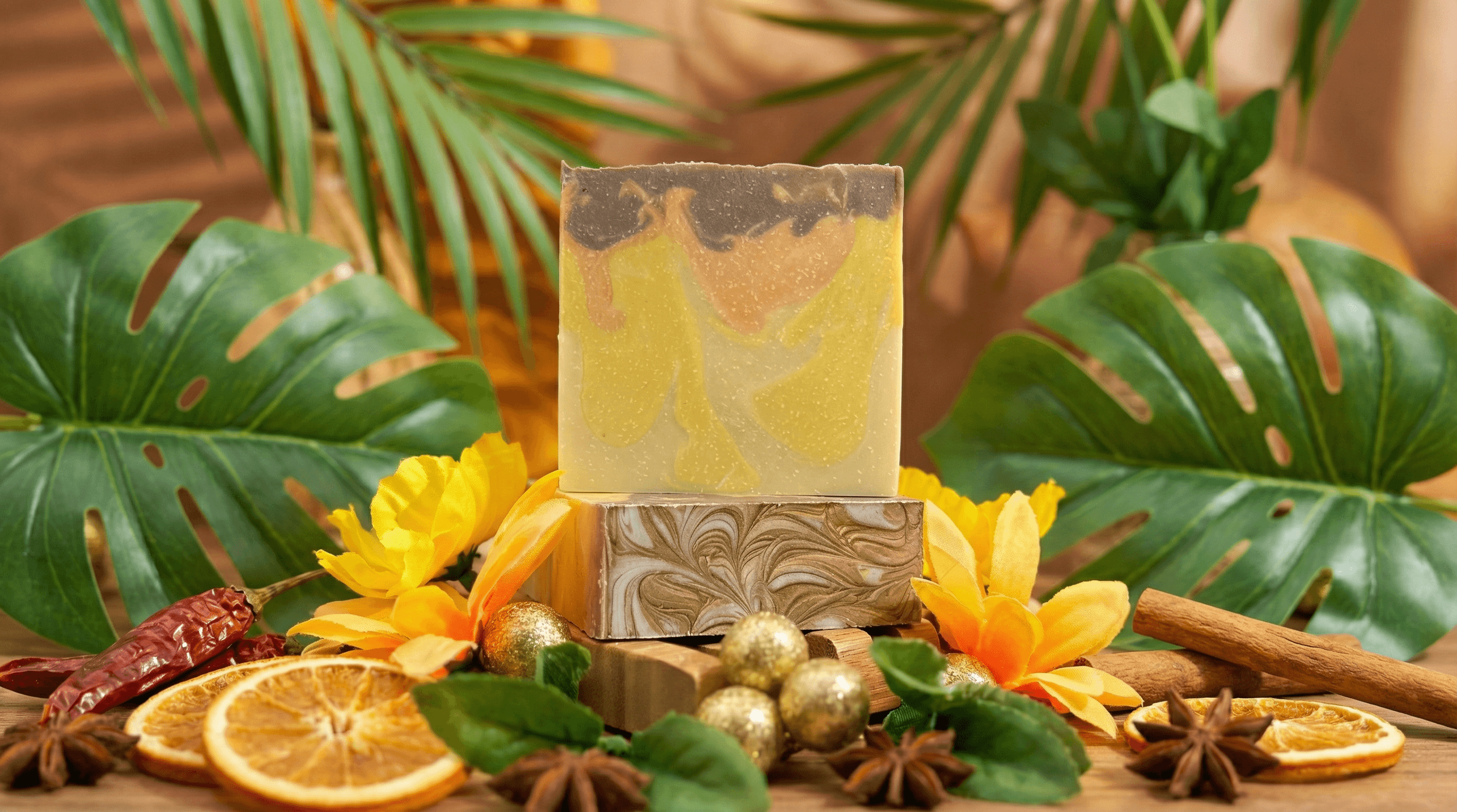 Handcrafted soap bar with swirled yellow, tan, and brown layers displayed on wooden pedestal, surrounded by dried orange slices, cinnamon sticks, star anise, and tropical leaves.